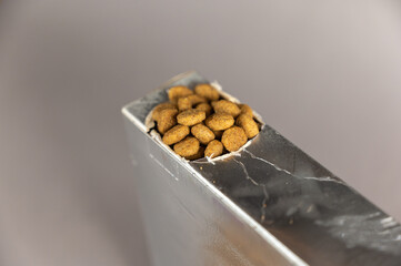 A silver rectangular box against a gray background. Pet food spilling out of the hole. Dry pelleted...