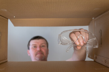 Man pulls safety glasses out of cardboard box for moving. Personal protective equipment. Bottom view. Inside view. Close-up. Selective focus.