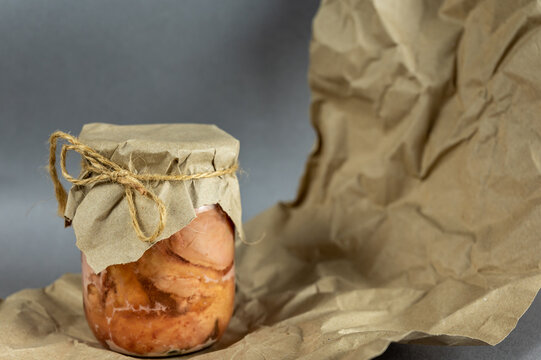 A glass jar of canned meat. Homemade stew in front of the gray background. Slices of appetizing meat tightly packed in a transparent jar. Food ready to eat. Close-up. Selective focus.