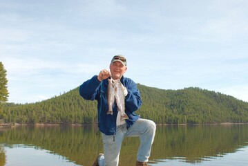 An angler with a stringer of trout on the edge of a lake 