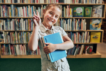 Back to school. Happy little girl at school again. Smiling student making V sign hand gesture...