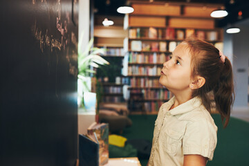 Little girl writing on blackboard. Smart student put solve on chalkboard. Back to school. Child...