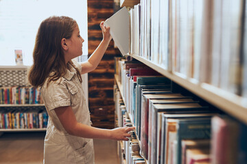 Schoolgirl choosing book in school library. Smart girl selecting books. Learning from books. School...