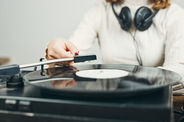 Young woman listening to music from vinyl record player. Playing music on turntable player. Female enjoying music from old record collection at home