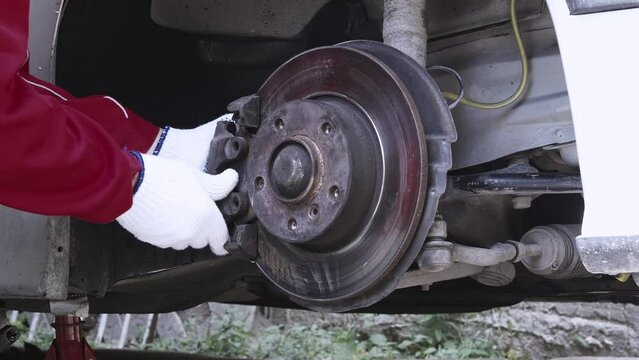Male hands of car mechanic wears uniform unscrews the brake pads, removing brake caliper. Vehicle maintenance