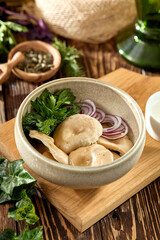 Traditional russian appetizer - salted milk mushrooms with onion. Pickled mushrooms with sour cream on bowl. Salted gruzdi on wooden background in rustic style. Lactarius with onion on wooden table.
