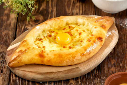 Traditional georgian pastry - adjarian khachapuri with cheese and raw yolk. Khachapuri with egg on wooden background in rustic style. Adjara khachapuri with ingredients. Georgian cuisine.