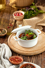 Beef ragout with vegetables in ceramic pot on wooden rustic background. Stew meat with coriander leaf on casserole in georgian style. Composition with meat ragout on wooden table with ingredients.