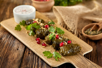 Traditional georgian food - meat dolma on plate with sauce in rustic style. Caucasian dish - stuffed grape leaves with minced meat and pomegranate on wooden background. Composition with meat dolma.