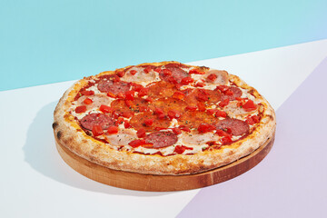 Italian pizza with salami, ham, pepperoni and paprika on coloured background. Meat pizza with salami and pepperoni in minimal style on blue color. American pizza delivery concept with color backdrop.