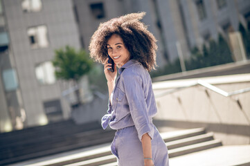 Pretty curly-haired woman walking in the street and talking on the phone