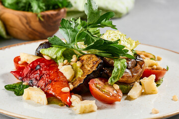Salad with grilled vegetables, greens and cheese on concrete background. Warm salad with paprika, zucchini, eggplant and tomato on grill. Aesthetic composition with veggie salad. Summer menu concept.