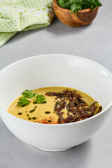 Cream soup with vegetables and crispy meat. Pea cream soup with spices on concrete background. Aesthetic composition with vegetables soup in white ceramic bowl