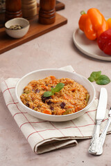 Grain dish - Millet with tomatoes, beans, carrots and spices, mint in a white bowl on a concrete round tray with checkered linen kitchen towel on purple background