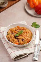 Grain dish - Millet with tomatoes, beans, carrots and spices, mint in a white bowl on a concrete round tray with checkered linen kitchen towel on purple background