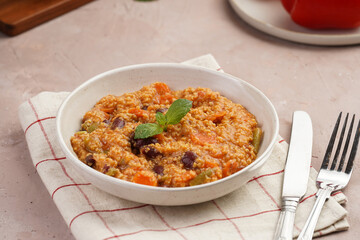 Grain dish - Millet with tomatoes, beans, carrots and spices, mint in a white bowl on a concrete round tray with checkered linen kitchen towel on purple background