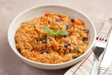 Grain dish - Millet with tomatoes, beans, carrots and spices, mint in a white bowl on a concrete round tray with checkered linen kitchen towel on purple background