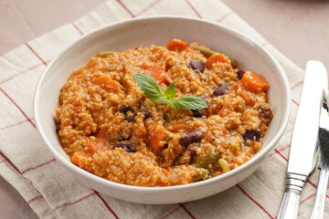 Grain dish - Millet with tomatoes, beans, carrots, bell pepper and spices, mint in a white bowl on...