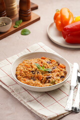 Grain dish - Millet with tomatoes, beans, carrots, bell pepper and spices, mint in a white bowl on a checkered linen kitchen towel on purple background