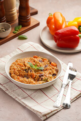 Grain dish - Millet with tomatoes, beans, carrots, bell pepper and spices, mint in a white bowl on a checkered linen kitchen towel on purple background