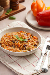 Grain dish - Millet with tomatoes, beans, carrots, bell pepper and spices, mint in a white bowl on a checkered linen kitchen towel on purple background