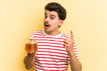 Young caucasian man holding honey jar isolated on yellow background having an idea, inspiration...