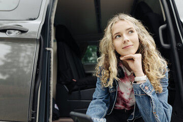 Fototapeta na wymiar Young teenager sitting in camping van with her cell phone and thinking