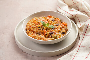 Grain dish - Millet with tomatoes, beans, carrots and spices, mint in a white bowl on a concrete round tray with checkered linen kitchen towel on purple background 