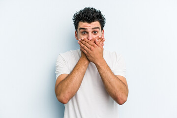 Young caucasian man isolated on blue background shocked covering mouth with hands.