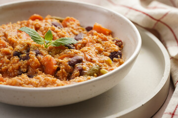 Grain dish - Millet with tomatoes, beans, carrots and spices, mint in a white bowl on a concrete...