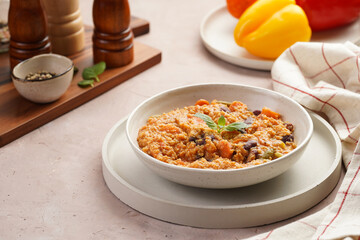 Grain dish - Millet with tomatoes, beans, carrots and spices, mint in a white bowl on a concrete round tray with checkered linen kitchen towel on purple background