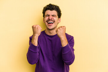 Young caucasian man isolated on yellow background cheering carefree and excited. Victory concept.