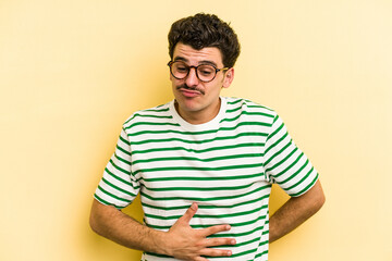 Obraz premium Young caucasian man isolated on yellow background touches tummy, smiles gently, eating and satisfaction concept.
