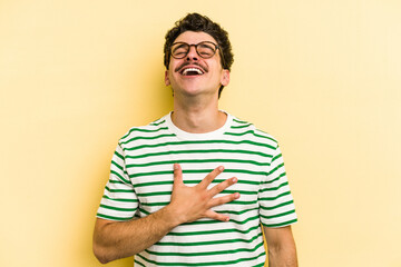 Young caucasian man isolated on yellow background laughs out loudly keeping hand on chest.