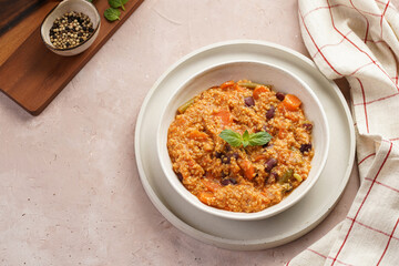 Grain dish - Millet with tomatoes, beans, carrots and spices, mint in a white bowl on a concrete round tray with checkered linen kitchen towel on purple background, top view
