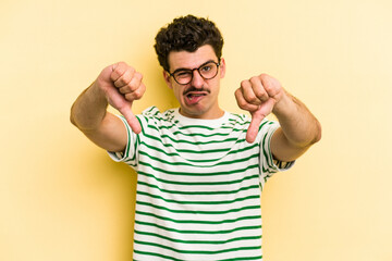 Fototapeta premium Young caucasian man isolated on yellow background showing thumb down and expressing dislike.