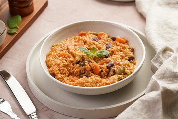 Grain dish - Millet with tomatoes, beans, carrots and spices, mint in a white bowl on a concrete round tray with checkered linen kitchen towel on purple background
