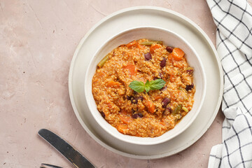 Grain dish - Millet with tomatoes, beans, carrots and spices, mint in a white bowl on a concrete round tray with checkered linen kitchen towel on purple background, top view
