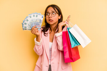 Young hispanic woman holding shopping bag isolated on yellow background