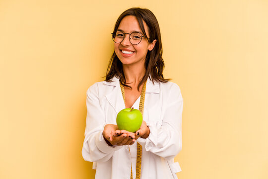 Young nutritionist woman holding a weighing machine isolated on yellow background