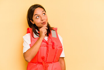 Young hispanic woman holding life jacket isolated on yellow background looking sideways with...
