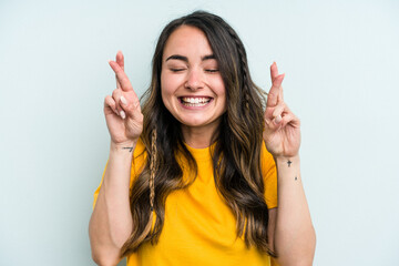 Young caucasian woman isolated on blue background crossing fingers for having luck