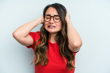 Young caucasian woman isolated on blue background covering ears with hands.