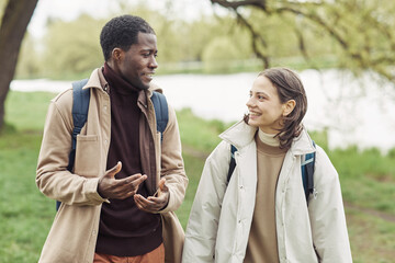 Happy multiethnic couple smiling to each other during conversation while they walking along the park