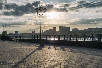 Panoramic view of evening city with golden sunset. Promenade embankment with street lamps