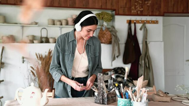 Smiling brunette woman listening music in headphones and prepares instruments in the workshop