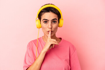 Young caucasian woman listening to music isolated on pink background keeping a secret or asking for silence.