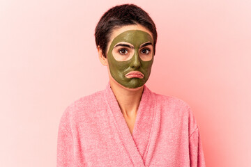 Young caucasian woman wearing a face mask isolated on pink background shrugs shoulders and open eyes confused.