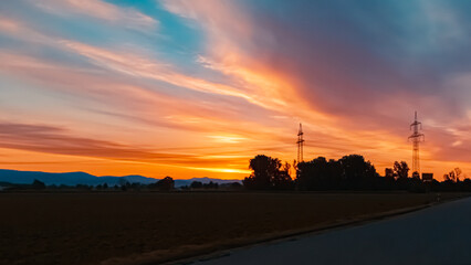 Beautiful sunset with a dramatic sky and overland high voltage lines near Tabertshausen, Bavaria, Germany