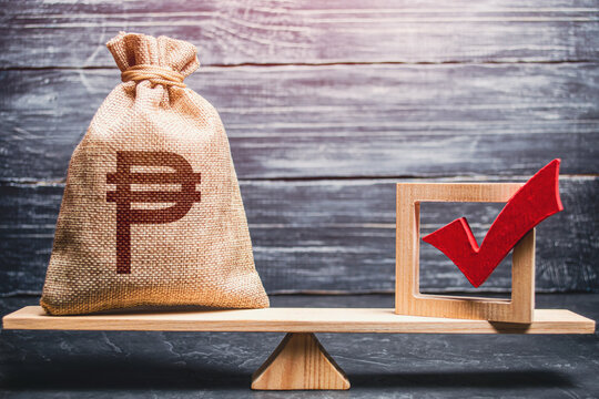 Red vote tick and a philippine peso money bag on scales. Concept of lobbying for decisions and laws. Estimating cost of making a decision and consequences in the future. Corruption risks.